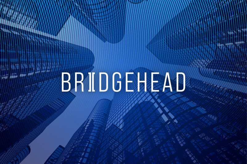 A view looking up at tall, modern skyscrapers with a blue digital overlay. The word "BRIDGEHEAD" is prominently displayed in white font in the center.