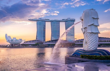 The iconic Merlion statue spouts water in the foreground, with the futuristic Marina Bay Sands and ArtScience Museum rising in the background against a vibrant sunset sky.