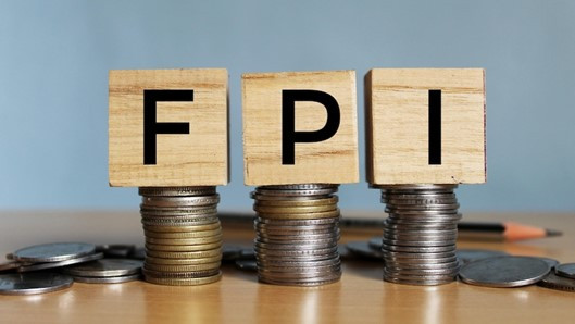 Three wooden blocks with the letters "F," "P," and "I" are stacked on top of piles of coins, symbolizing financial investment concepts. A pencil is partially visible in the background.