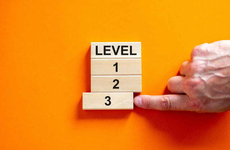 A hand pointing at a wooden block labeled "3," positioned below blocks labeled "LEVEL," "1," and "2," on a bright orange background.