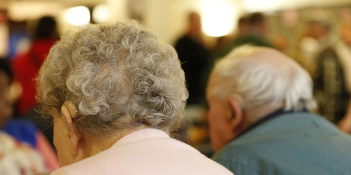 Close-up of the backs of two elderly individuals sitting together, showcasing their gray and curly hair in a bustling social setting.