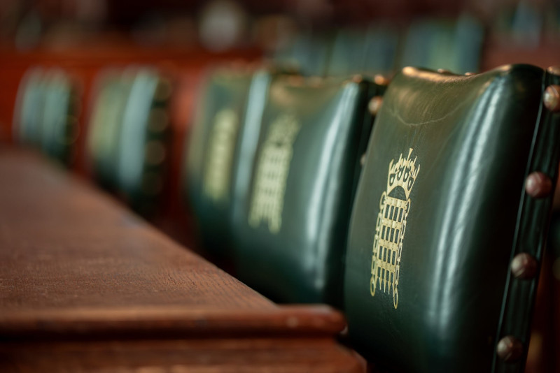 Green leather chairs with gold detailing are lined up in a historical chamber, with a polished wooden table in the foreground.