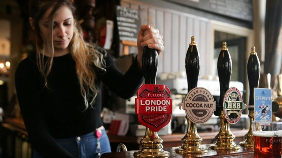 A bartender pulls a pint at a bar, showcasing various beer taps, including Fuller's London Pride, Cocoa Nut, and an IPA.