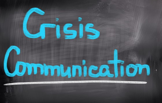 The words "Crisis Communication" are written in bright blue chalk on a black chalkboard.