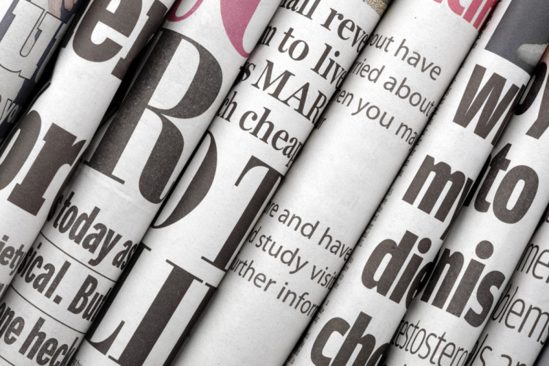 Close-up of rolled newspapers featuring various headlines and text in bold typography.