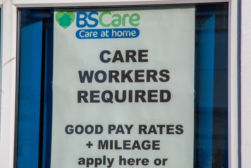 Sign displaying a job advertisement for care workers, mentioning good pay rates and mileage, with instructions to apply.