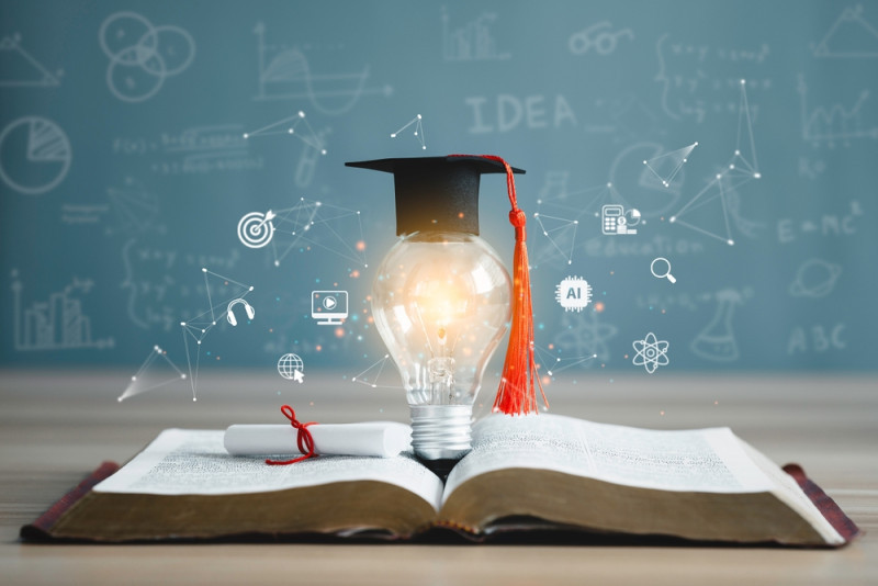A graduation cap sits atop a glowing light bulb resting on an open book. Surrounding the light bulb are icons representing education, technology, and science, with a chalkboard background filled with various mathematical and scientific symbols.