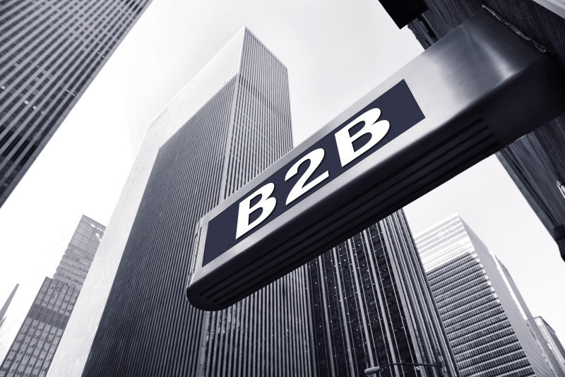 A street sign displaying "B2B" hangs above a modern cityscape with tall skyscrapers in black and white.