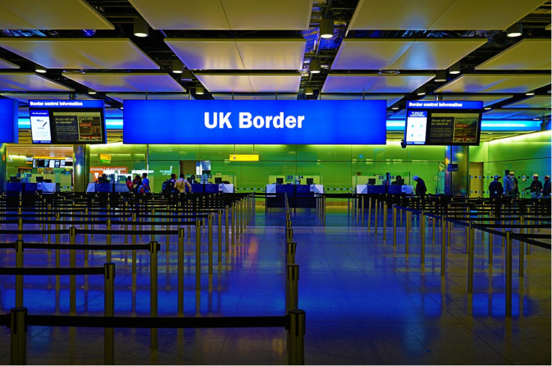 Empty immigration hall at the UK Border with queue barriers and illuminated signage.