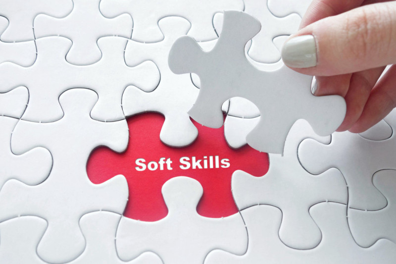 A hand holds a white puzzle piece above a jigsaw puzzle with a red piece marked "Soft Skills" that remains unfilled.