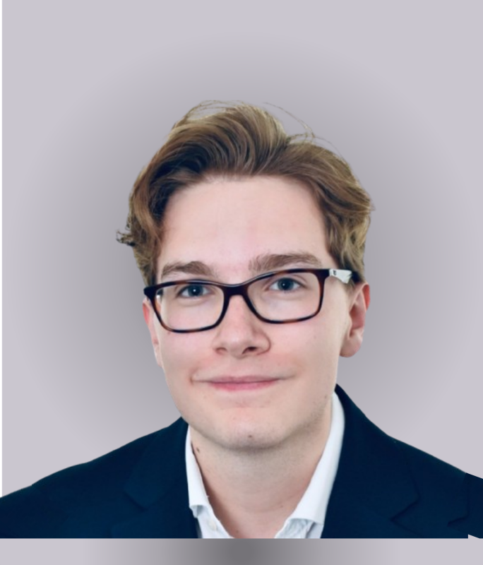 Young man with glasses and light brown hair, wearing a black suit jacket and a white shirt, smiling against a neutral background.